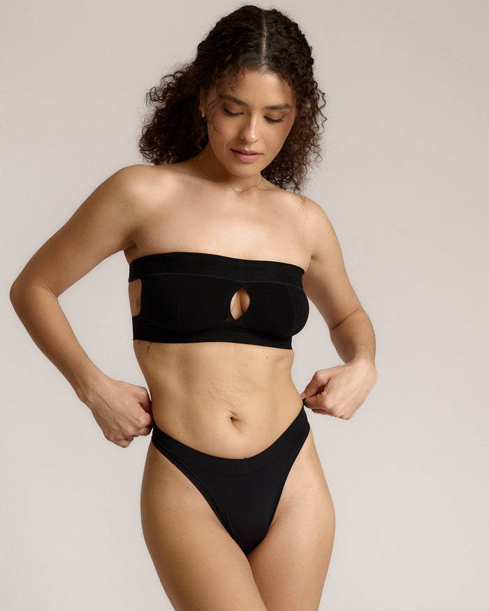 Woman wearing black strapless system against a neutral background