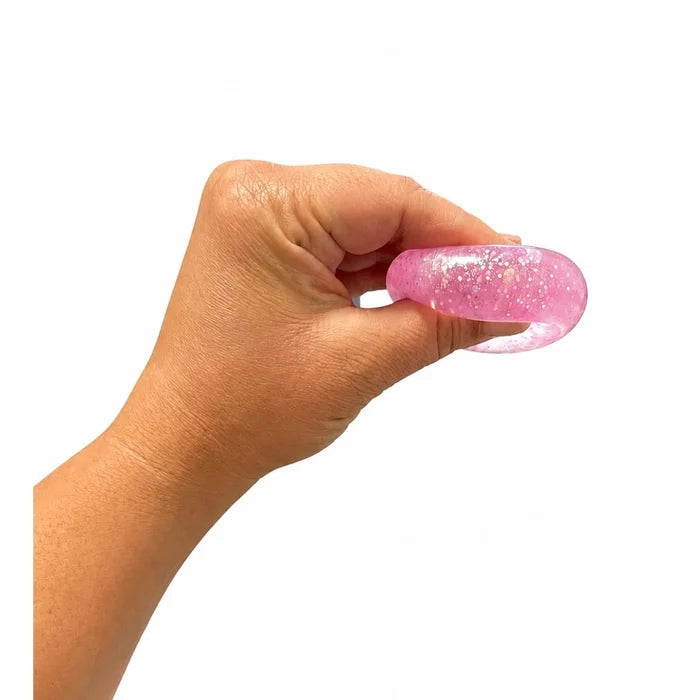 A hand holding a small, pink, translucent gel-like stress toy filled with gold glitter against a plain white background.