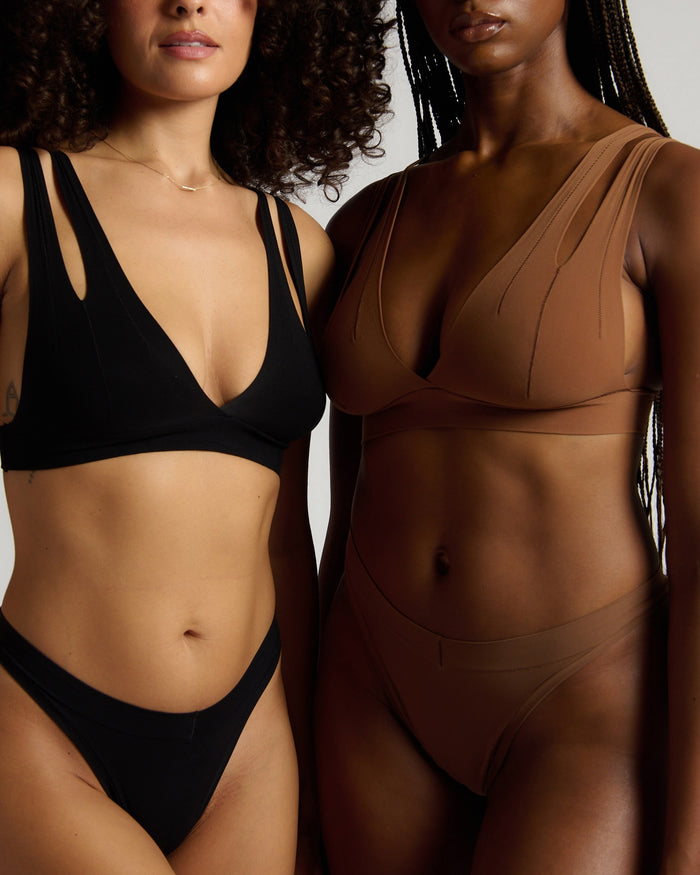 Two women wearing black and brown bras against a neutral background