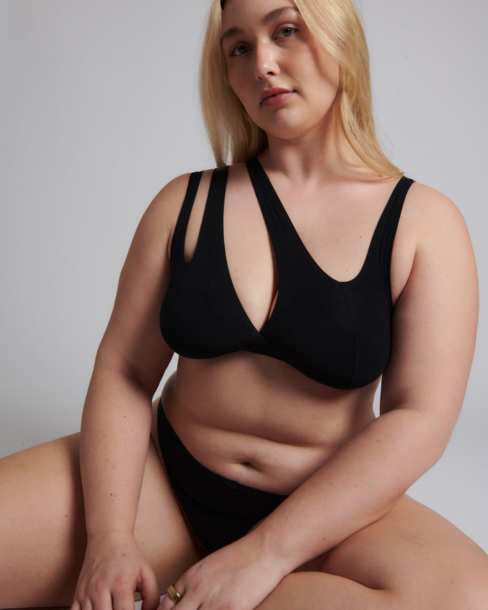 A woman sitting and wearing a black bra and matching panty set with a deep v-neckline.