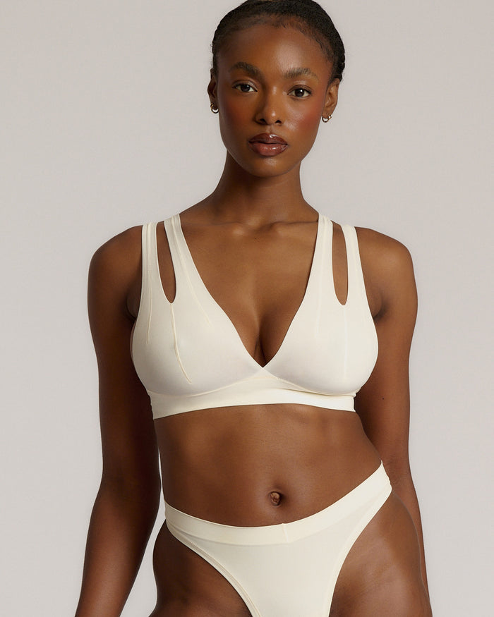A person wearing a white, solid-colored bra and matching thong, with unique strap details and a v-neckline.