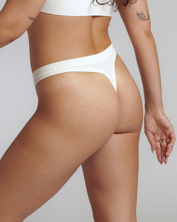 Close-up of a white thong underwear with a minimalist design, showing the waistband and part of the legs. The product is made from a stretchy fabric and appears to be smooth and comfortable.