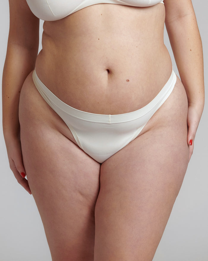 Close-up of a white thong underwear with a minimalist design, showing the waistband and part of the legs. The product is made from a stretchy fabric and appears to be smooth and comfortable.