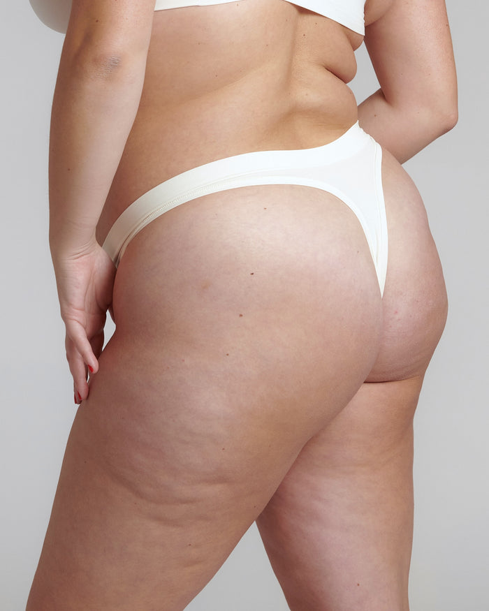 Close-up of a white thong underwear with a minimalist design, showing the waistband and part of the legs. The product is made from a stretchy fabric and appears to be smooth and comfortable.