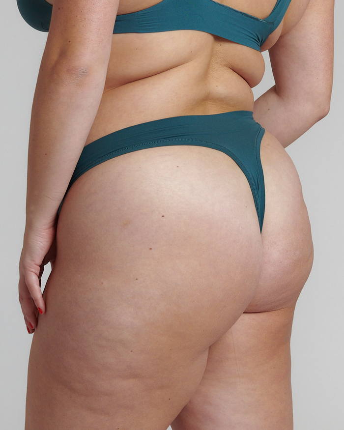 A person wearing a green thong underwear, the product is cut off at the waist and the person's legs are visible.