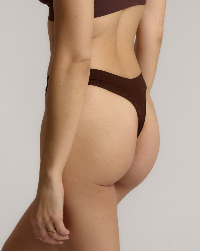 A woman wearing a brown thong on a plain background