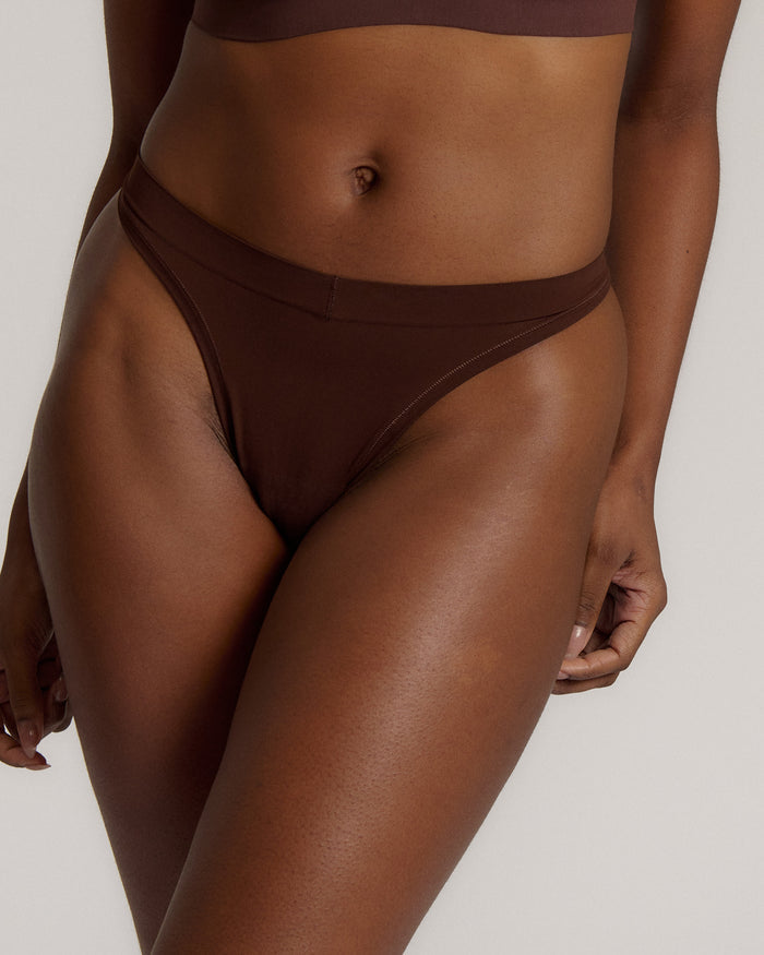 A woman wearing a brown thong on a plain background