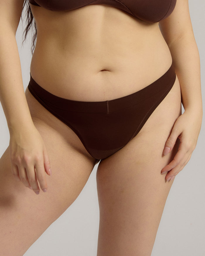 A woman wearing a brown thong on a plain background