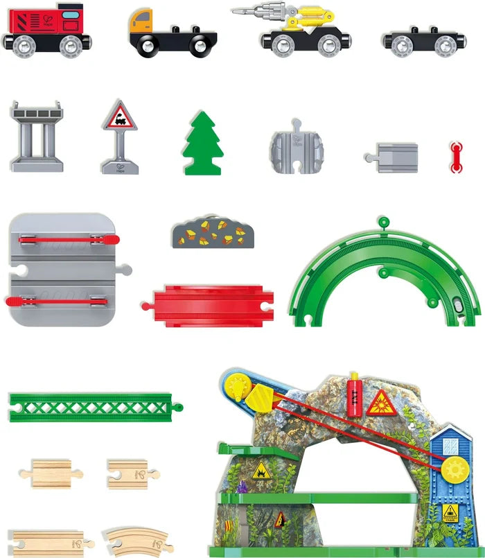 A set of colorful toy train tracks and accessories arranged on a white background, including trains, tracks, bridges, signals, a tree, rocks, and a small mountain train layout.