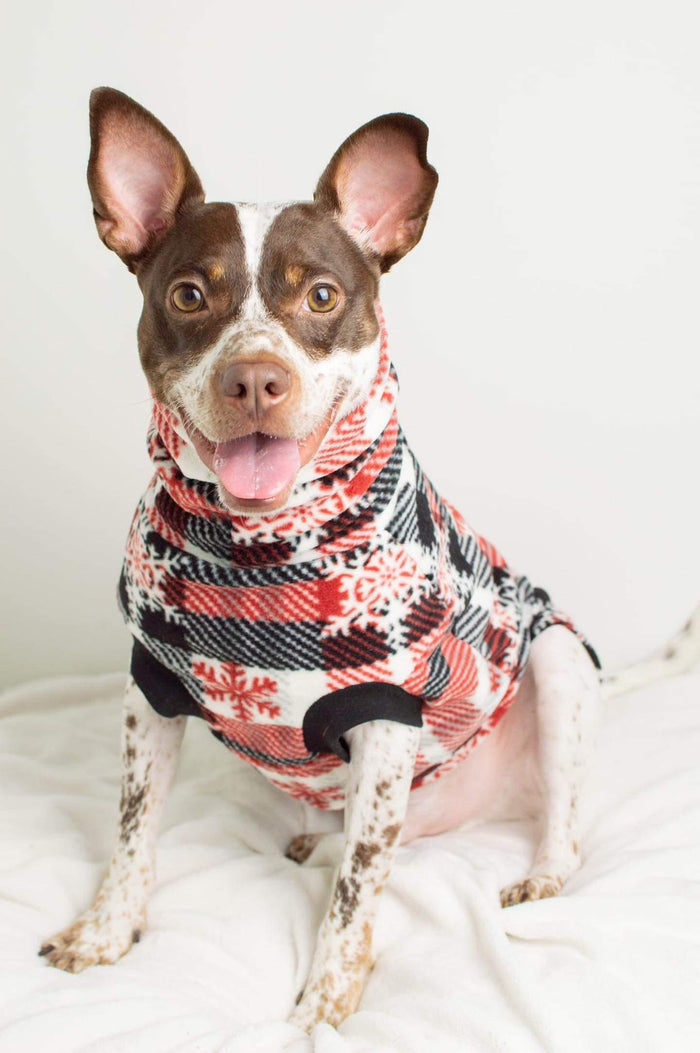 Red & black snowflake plaid fleece dog sweater worn by dog sitting on bed