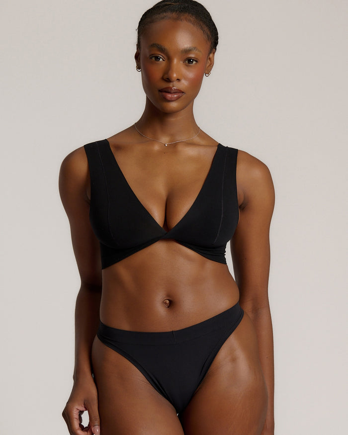 Woman wearing a black twist system and thong against a plain background