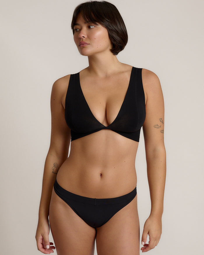 Woman wearing a black twist system and thong against a plain background