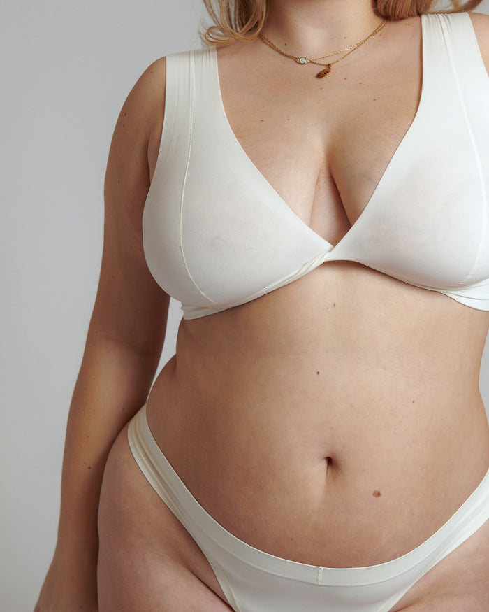 A person wearing a white, minimal-strap, twisted front bra and matching thong.