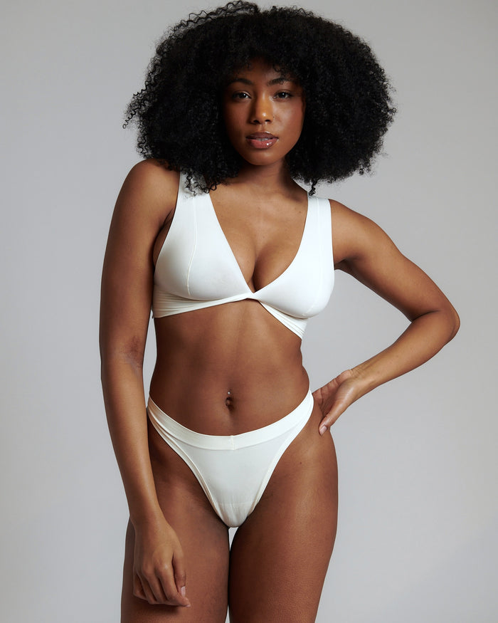 A person wearing a white, minimal-strap, twisted front bra and matching thong.