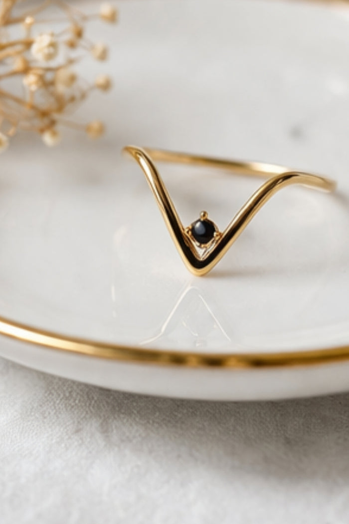v-shaped black onyx gold ring close-up on white plate minimal jewelry styling