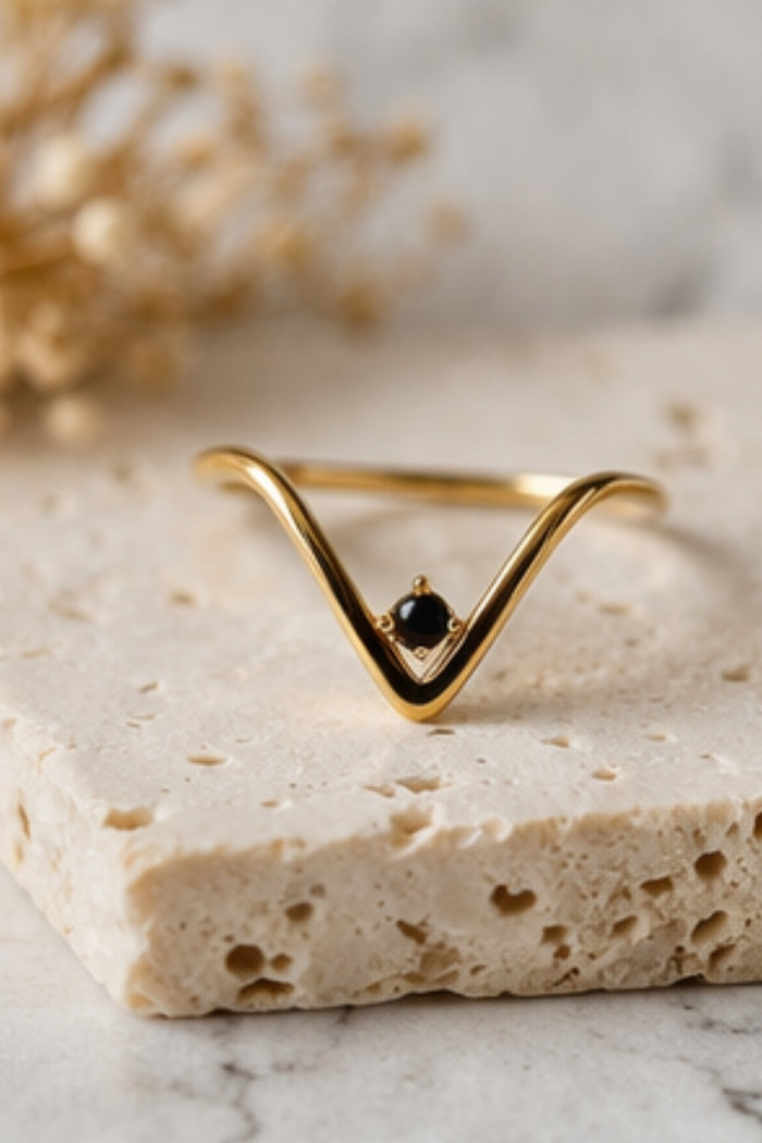 v-shaped black onyx gold ring close-up on textured stone surface neutral background
