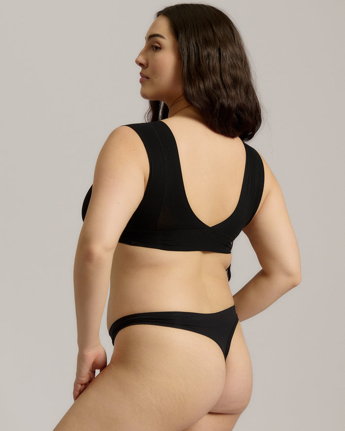 A woman wearing a black minimalist bra with wide straps and a deep neckline.