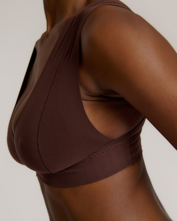 A woman wearing a brown Vii System bra, which is designed with a deep neckline, wide straps, and a smooth back.