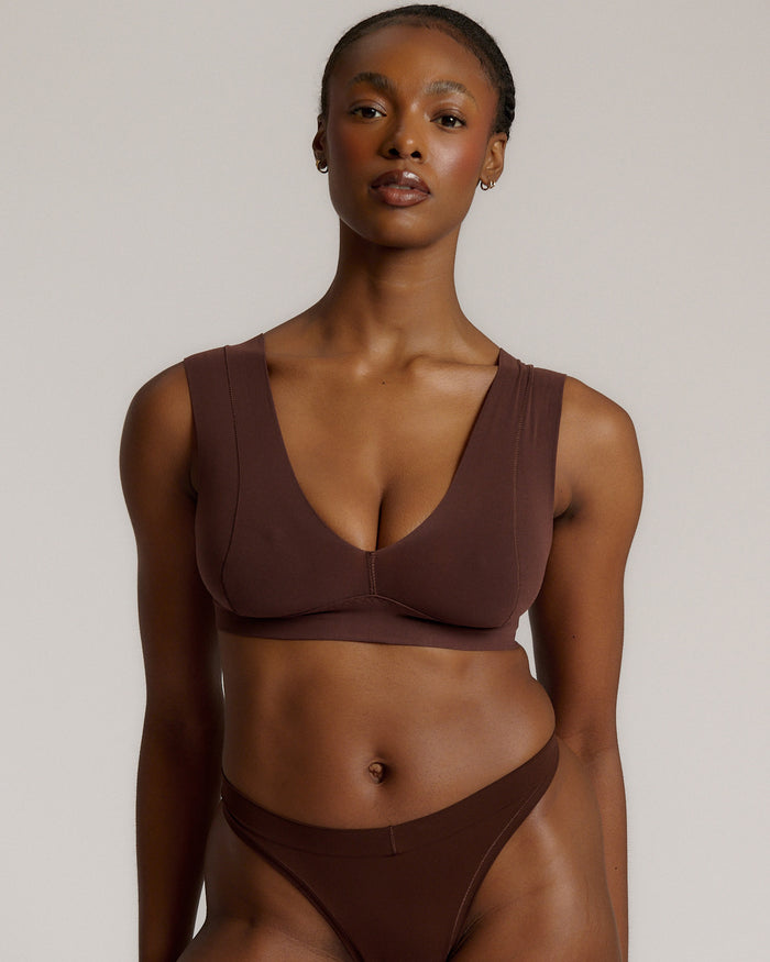 A woman wearing a brown Vii System bra, which is designed with a deep neckline, wide straps, and a smooth back.