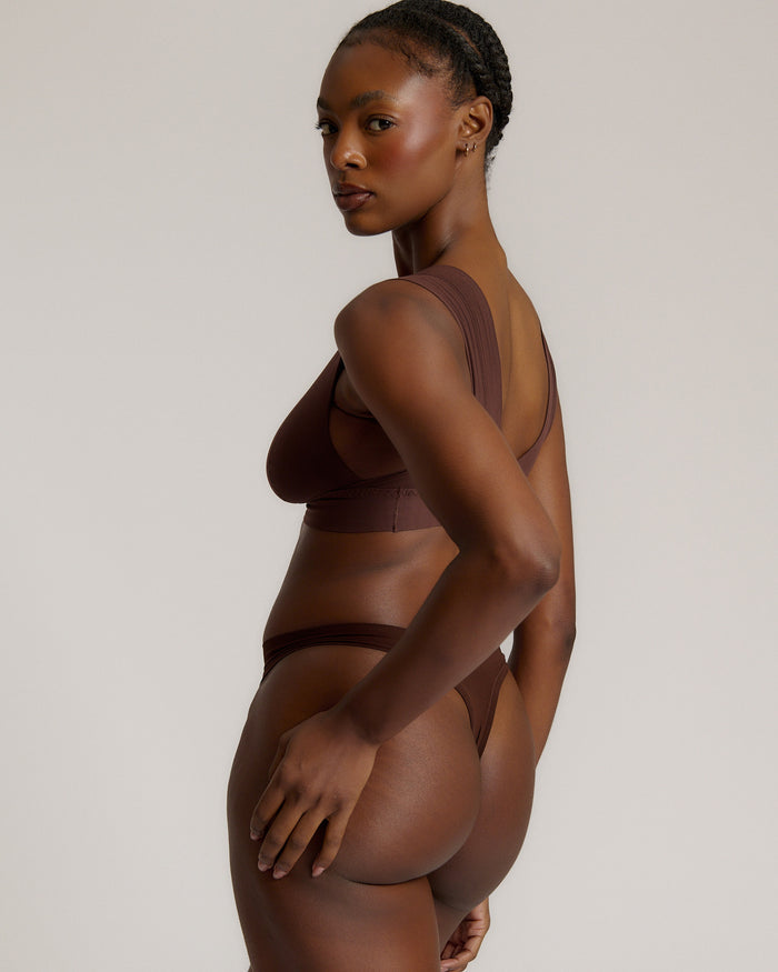 A woman wearing a brown Vii System bra, which is designed with a deep neckline, wide straps, and a smooth back.