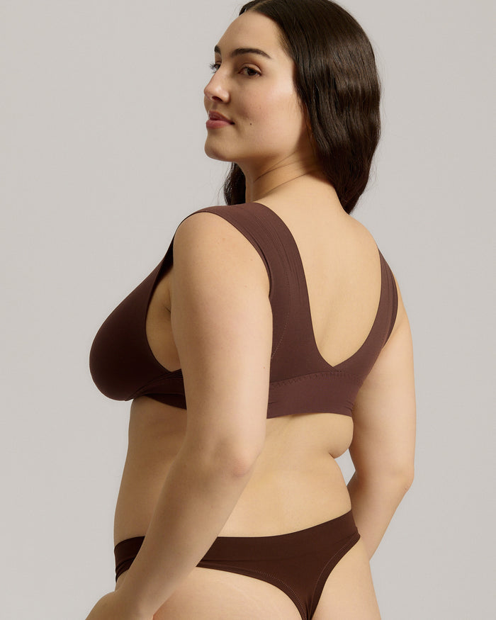 A woman wearing a brown Vii System bra, which is designed with a deep neckline, wide straps, and a smooth back.