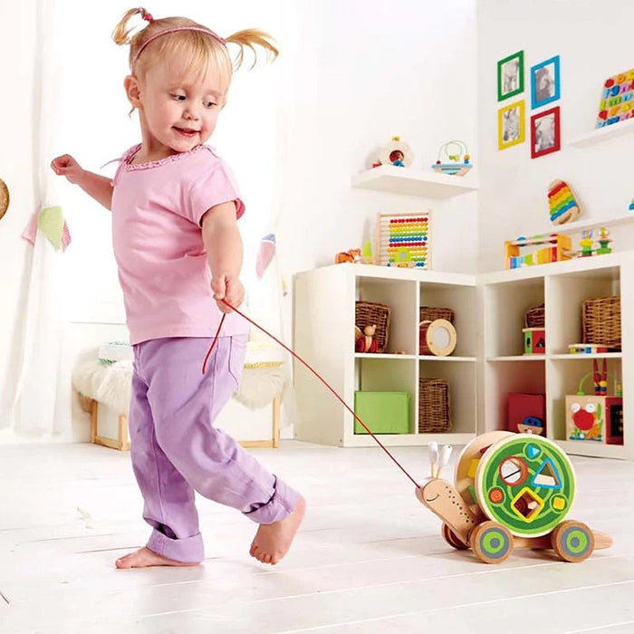 Child playing with the colorful Walk Along Snail in a room filled with books and toys.
