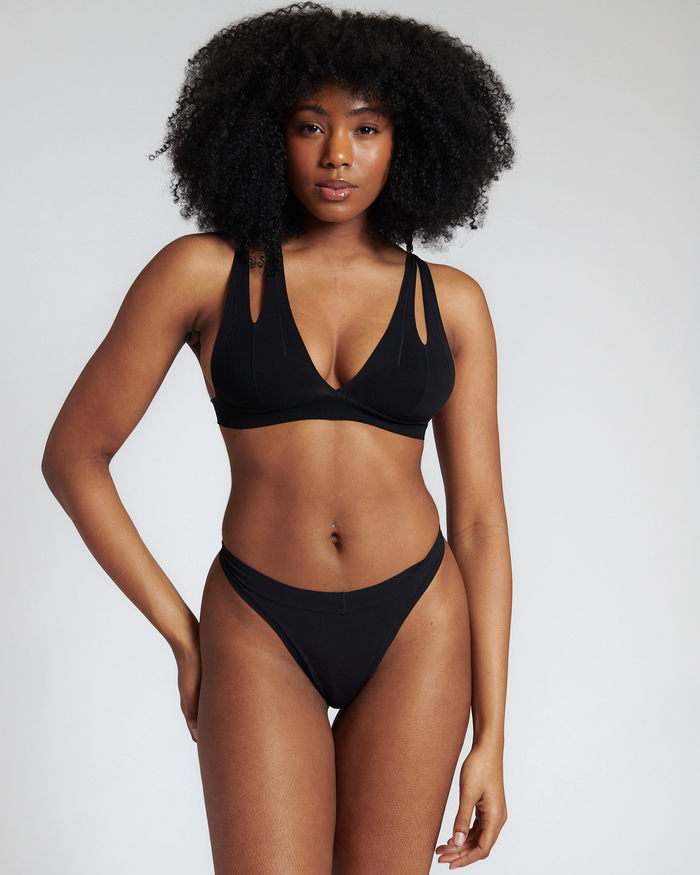 A person wearing a black x back system and black thong on a plain background.