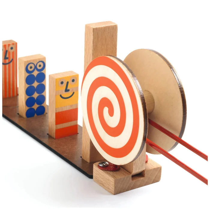 A wooden toy machine with colorful block characters, a spiral lollipop target, and red elastic bands on a white background.
