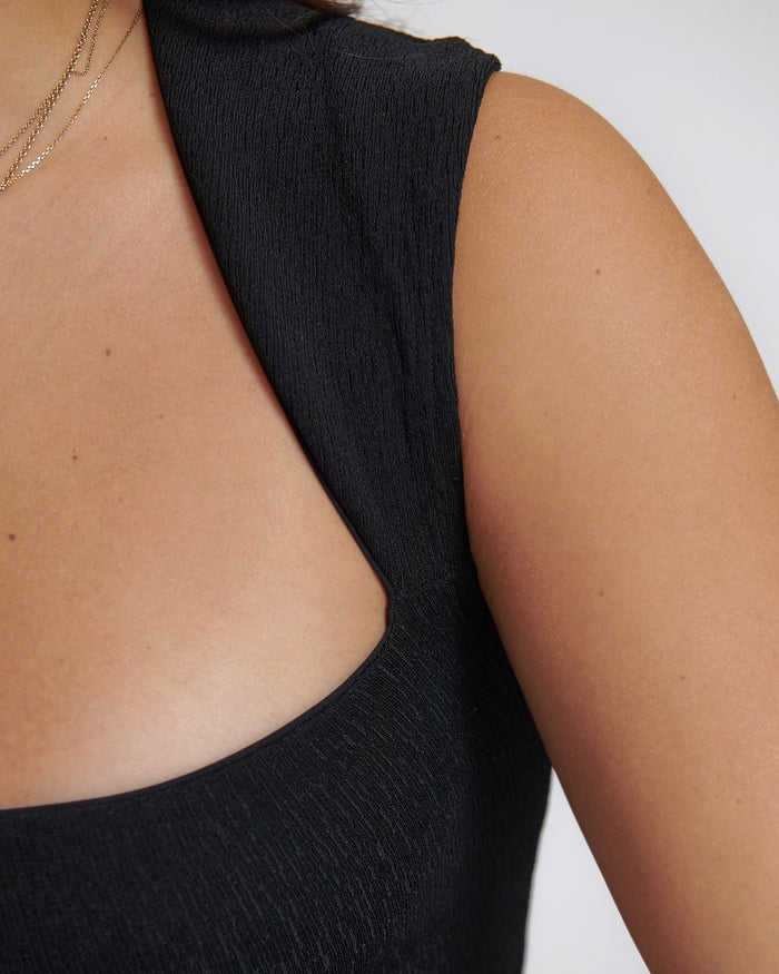 A woman wearing a black tank top with a square neck, designed to be versatile and stylish.