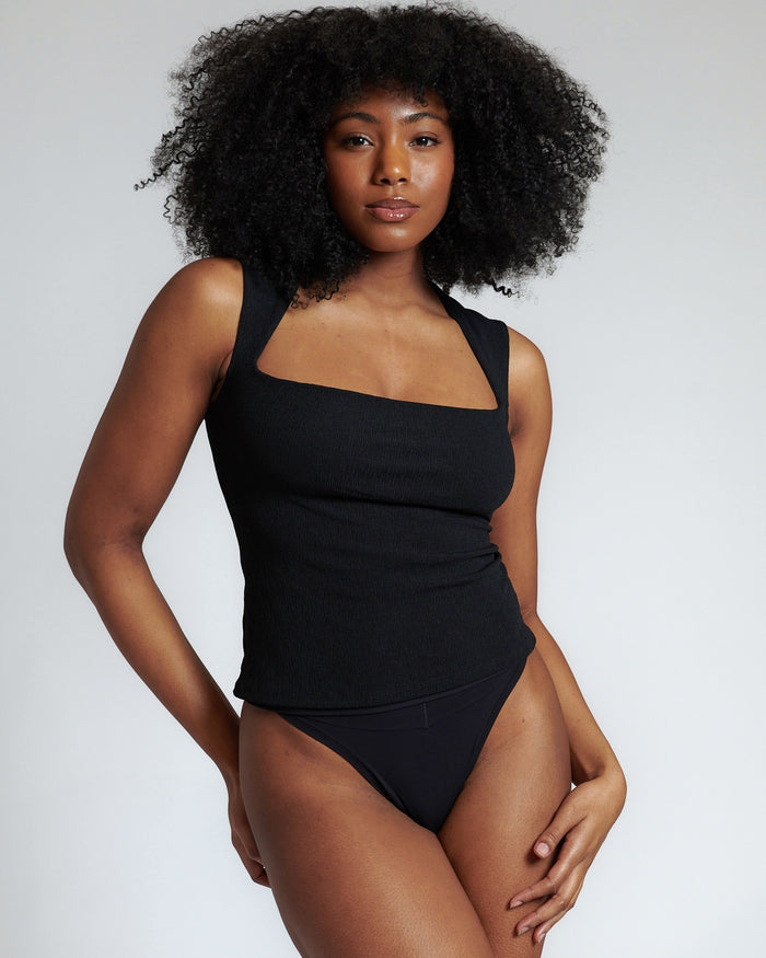 Woman wearing a black tank top and underwear on a light gray background