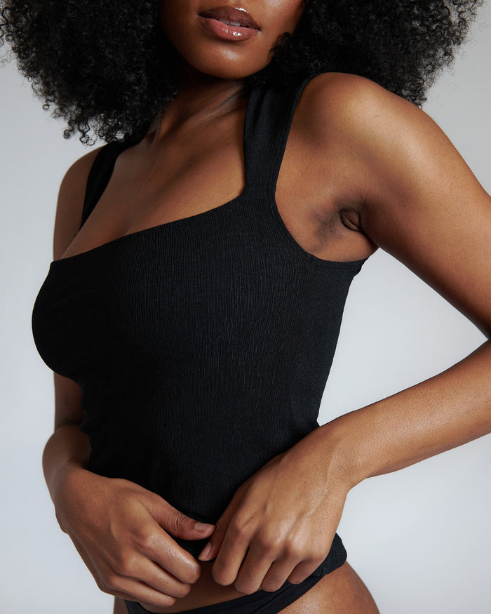 A woman wearing a black tank top with a square neck, designed to be versatile and stylish.